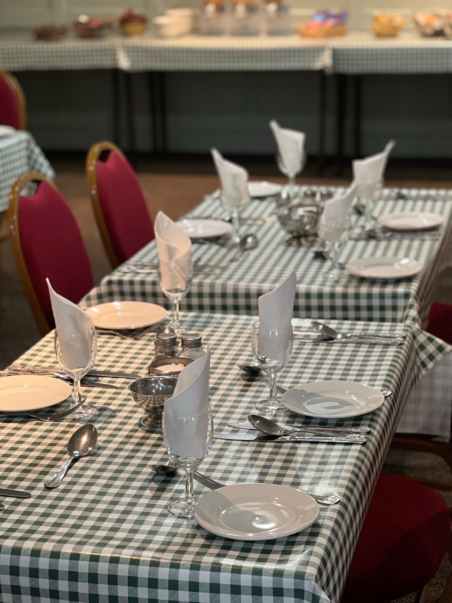 A dining area with checkered tablecloths, neatly set tables with plates, glasses, and cutlery.