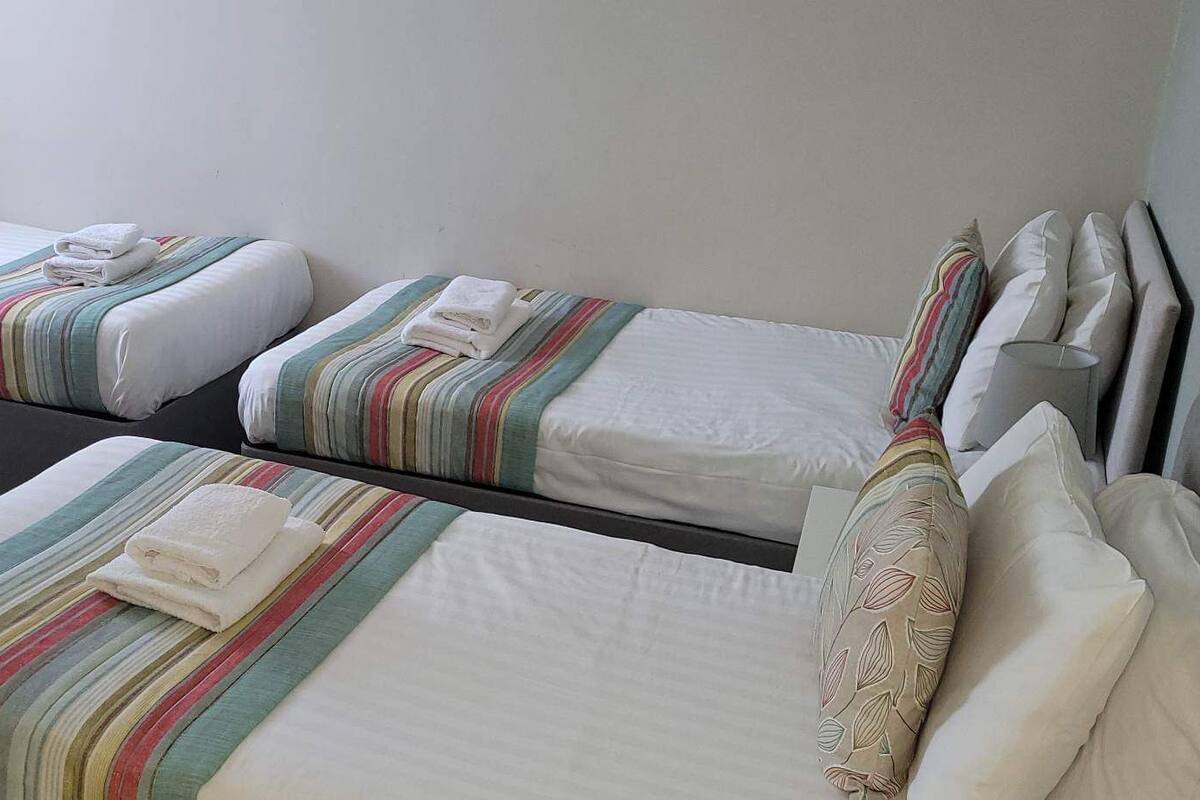 A hotel room with two single beds, each with striped bedding and pillows, a small bedside table, and a nightstand.