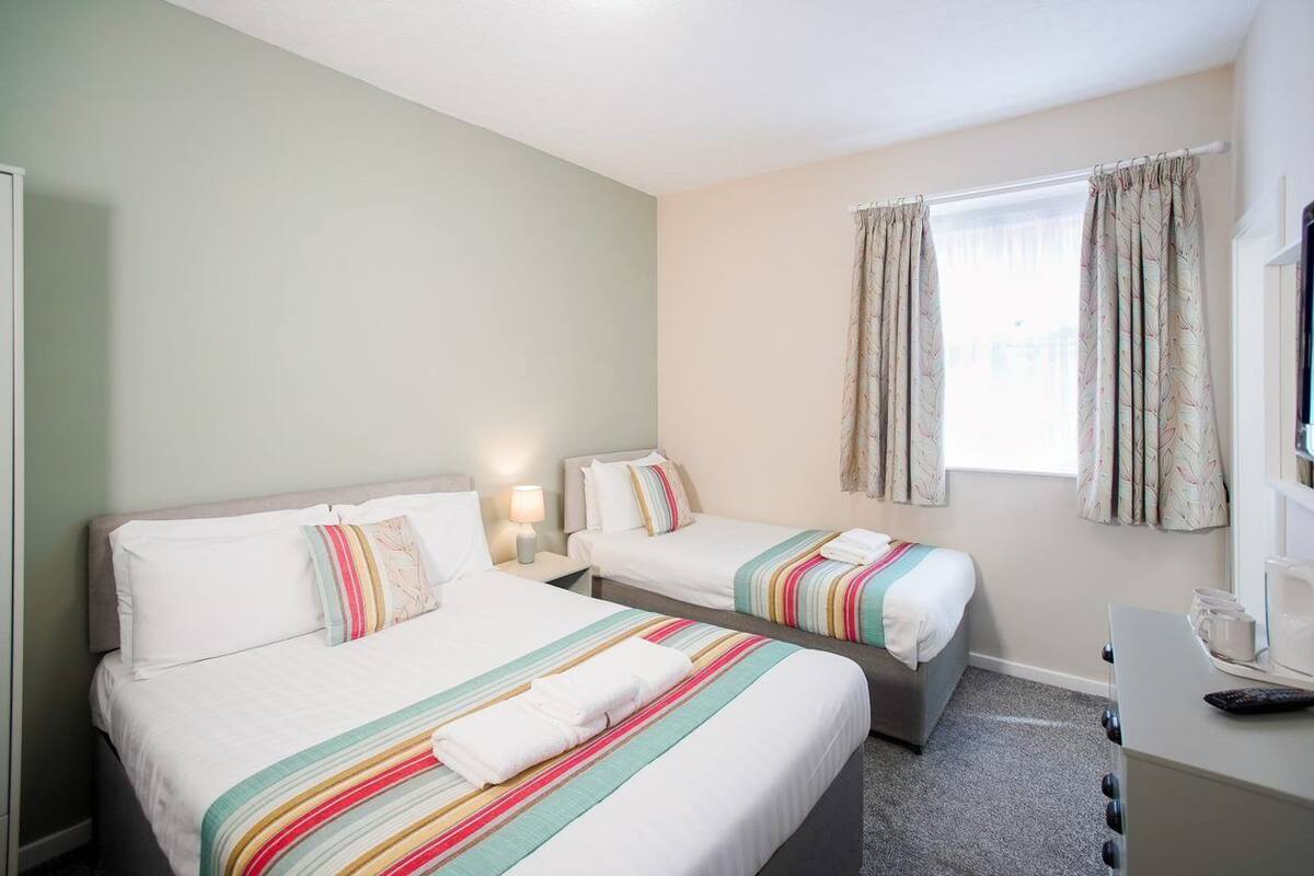 A hotel room with two single beds, a desk with a computer, and a window with curtains.