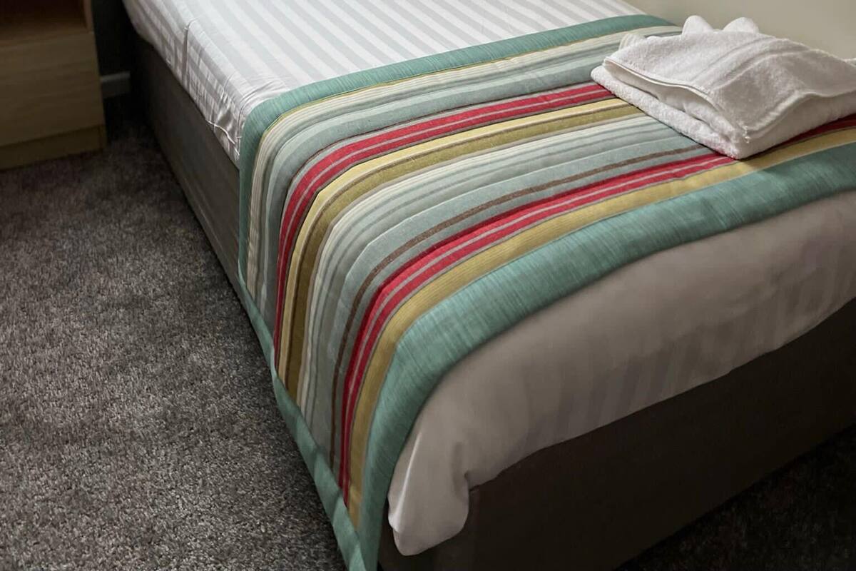 A single bed with a striped blanket, two pillows, a wooden headboard, and a nightstand.