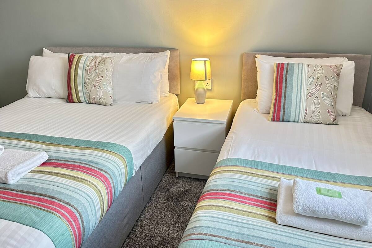A hotel room with two beds, each with striped bedding and decorative pillows. There is a nightstand with a lamp between the beds.