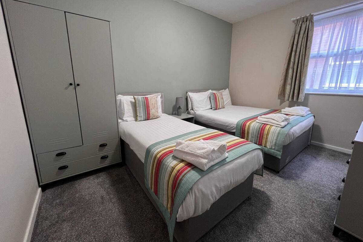 A room with two single beds, a wardrobe, a desk, and a window with curtains.