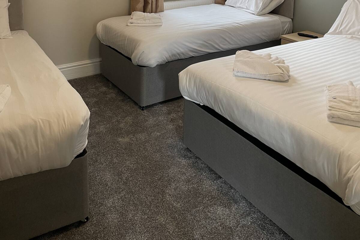 A hotel room with two single beds, a window with curtains, a small bedside table, and a carpeted floor.