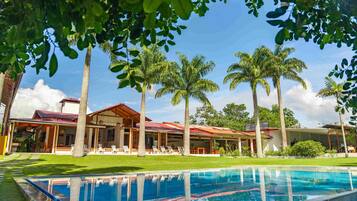 Piscina com água cristalina, cercada por palmeiras e um edifício com telhado vermelho.