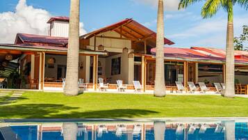 Resort com piscina, palmeiras e área de varanda coberta.