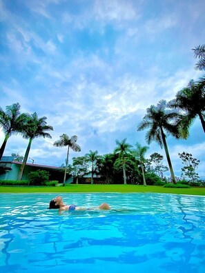 A swimming pool with a person lying on the edge, surrounded by palm trees and a clear sky. -  Altavista Casahotel - Asociado Casa Andina (Moyobamba)