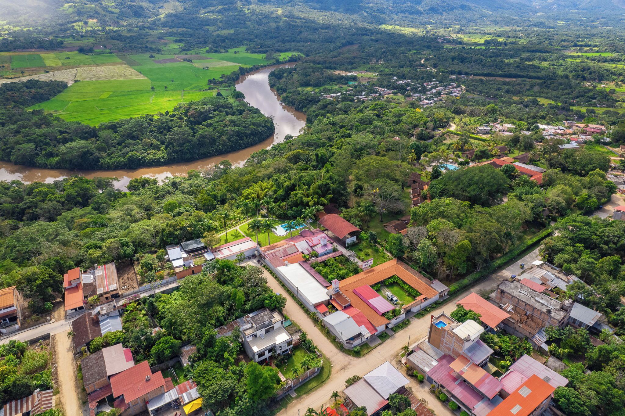 An aerial view of a residential area with houses, a river, and surrounding greenery.