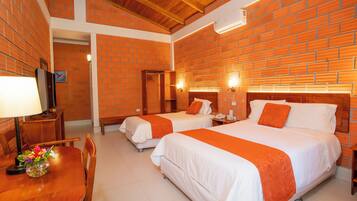 Habitación de hotel con dos camas, techo de madera, paredes de ladrillo, un escritorio con silla y televisor.