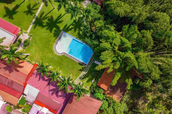 An aerial view of a residential area with a swimming pool surrounded by lush greenery and palm trees. -  Altavista Casahotel - Asociado Casa Andina (Moyobamba)