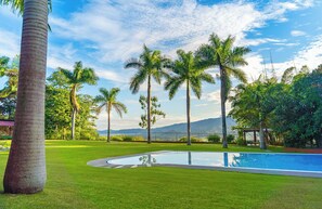Una piscina rodeada de palmeras y un área verde con una montaña al fondo.