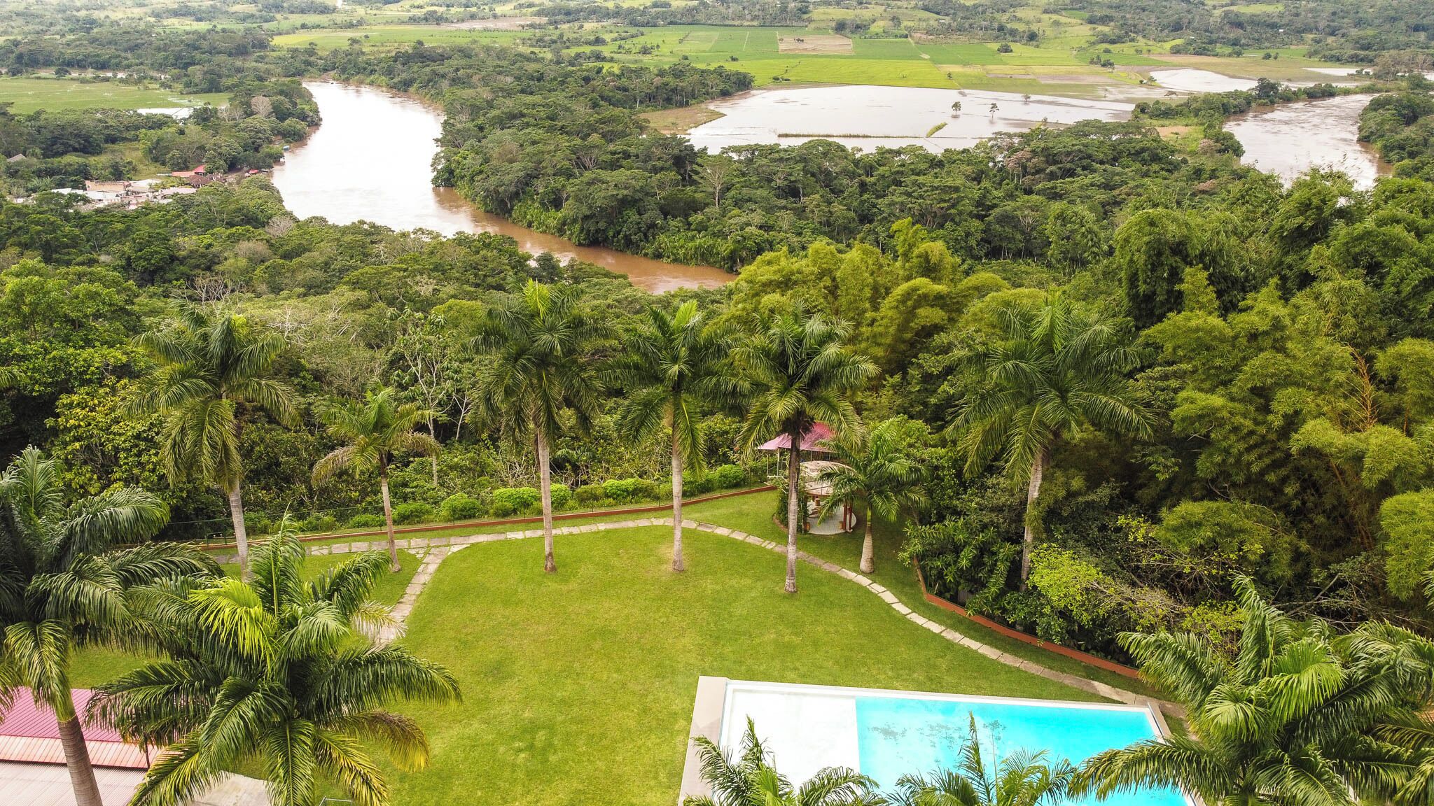 A lush landscape with a river, palm trees, and a swimming pool.
