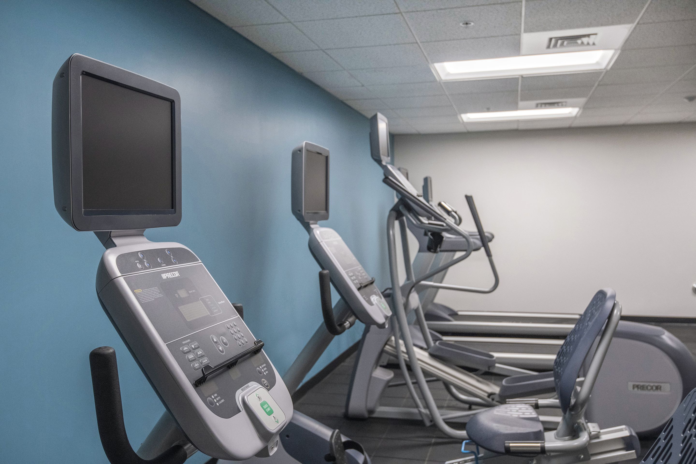 An exercise room with treadmills and a stationary bike, equipped with digital displays and control panels.