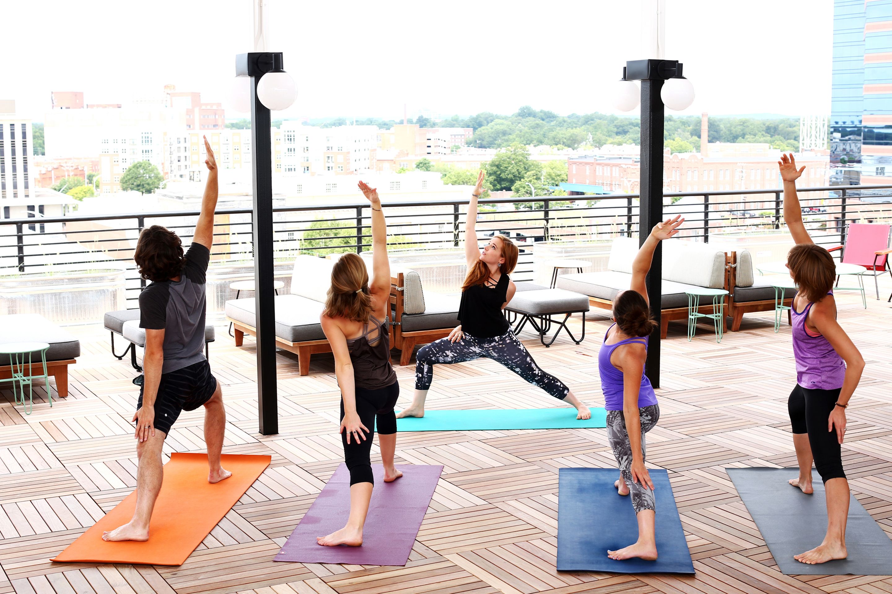 Un groupe de personnes pratiquant le yoga sur des tapis à l’extérieur, avec une vue sur la ville en arrière-plan.