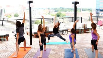 Un groupe de personnes pratiquant le yoga sur des tapis à l’extérieur, avec une vue sur la ville en arrière-plan.
