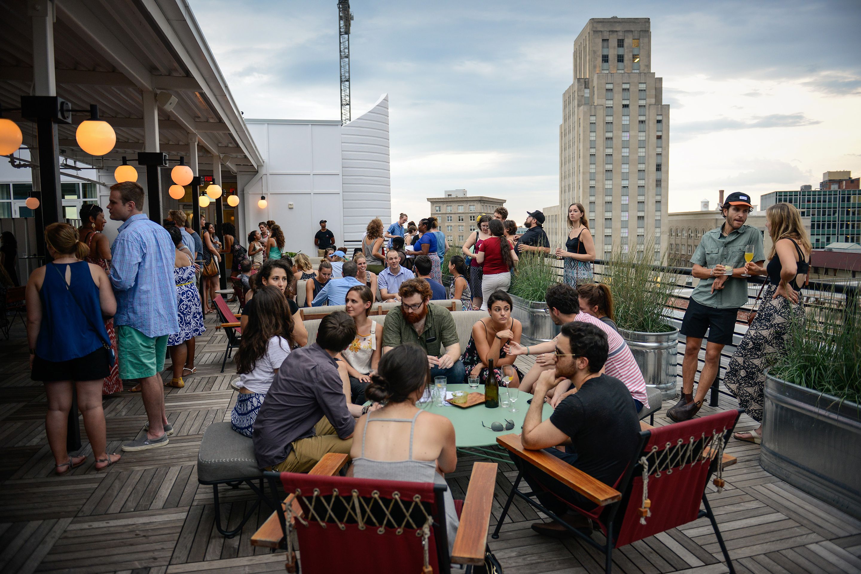 A rooftop bar with outdoor seating, surrounded by city buildings, under a cloudy sky.