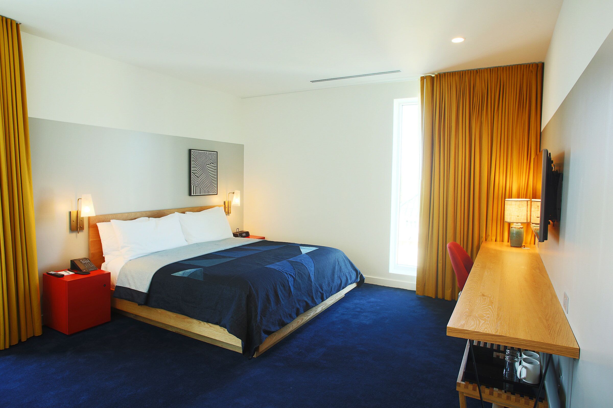 Een hotelkamer met een bed, een bureau en een stoel. Op het bureau staat een lamp en op het nachtkastje een telefoon.