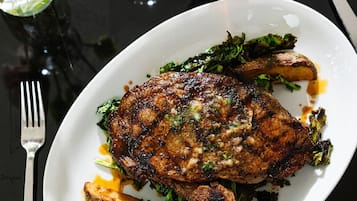 Une assiette contenant de la viande grillée, des légumes et un verre d’une boisson rouge, le tout posé sur une table.