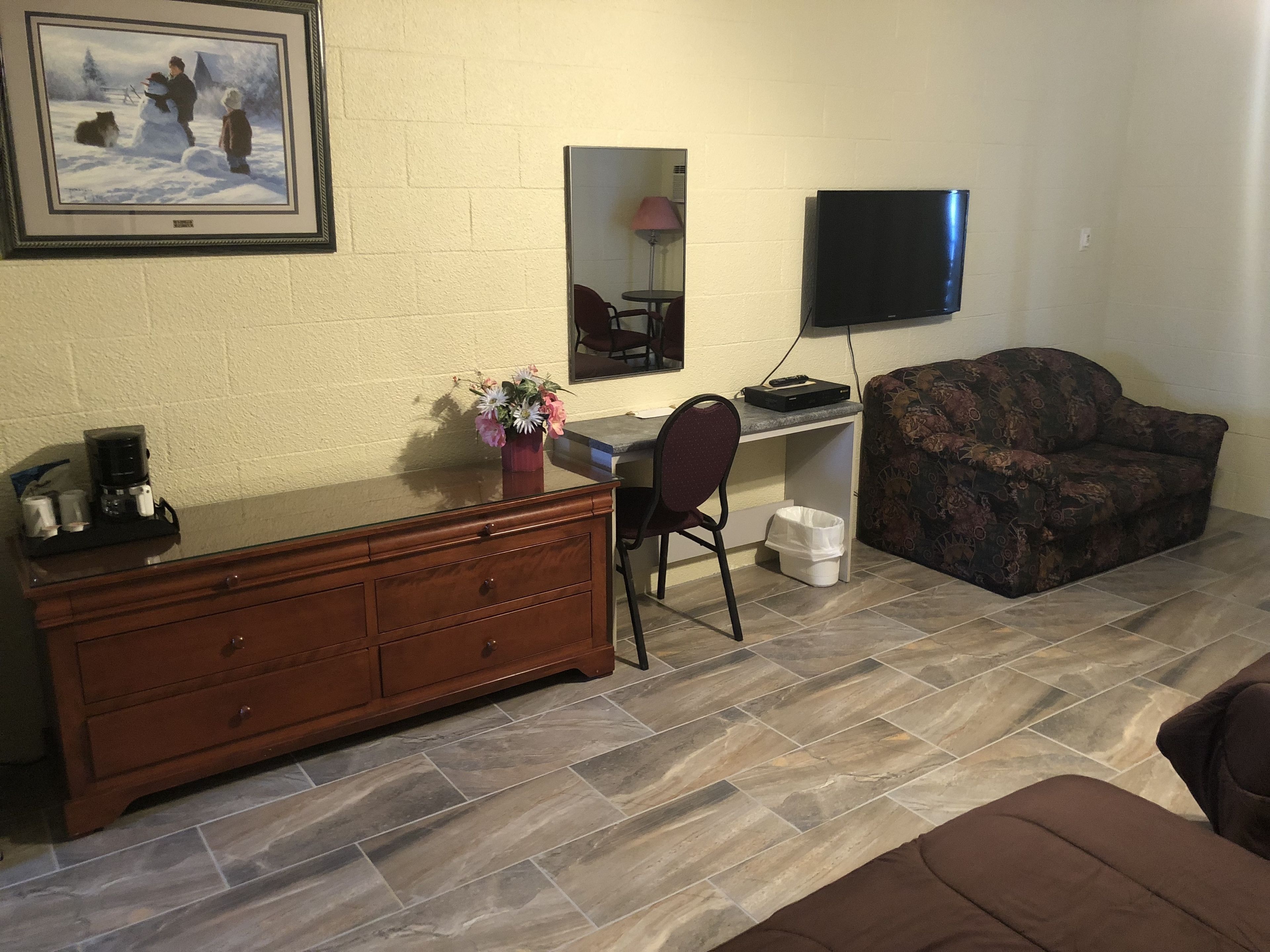 A living room with a wooden dresser, a desk with a computer, a couch, and a TV mounted on the wall.