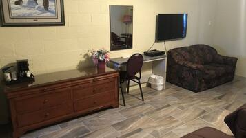 A living room with a wooden dresser, a desk with a computer, a couch, and a TV mounted on the wall.