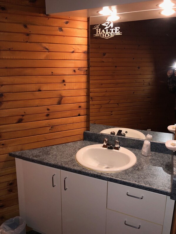 Un baño con paredes de madera, un lavamanos blanco y un espejo.