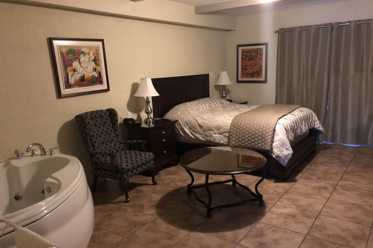 A hotel room with a bed, a chair, a table, a lamp, and a bathtub.