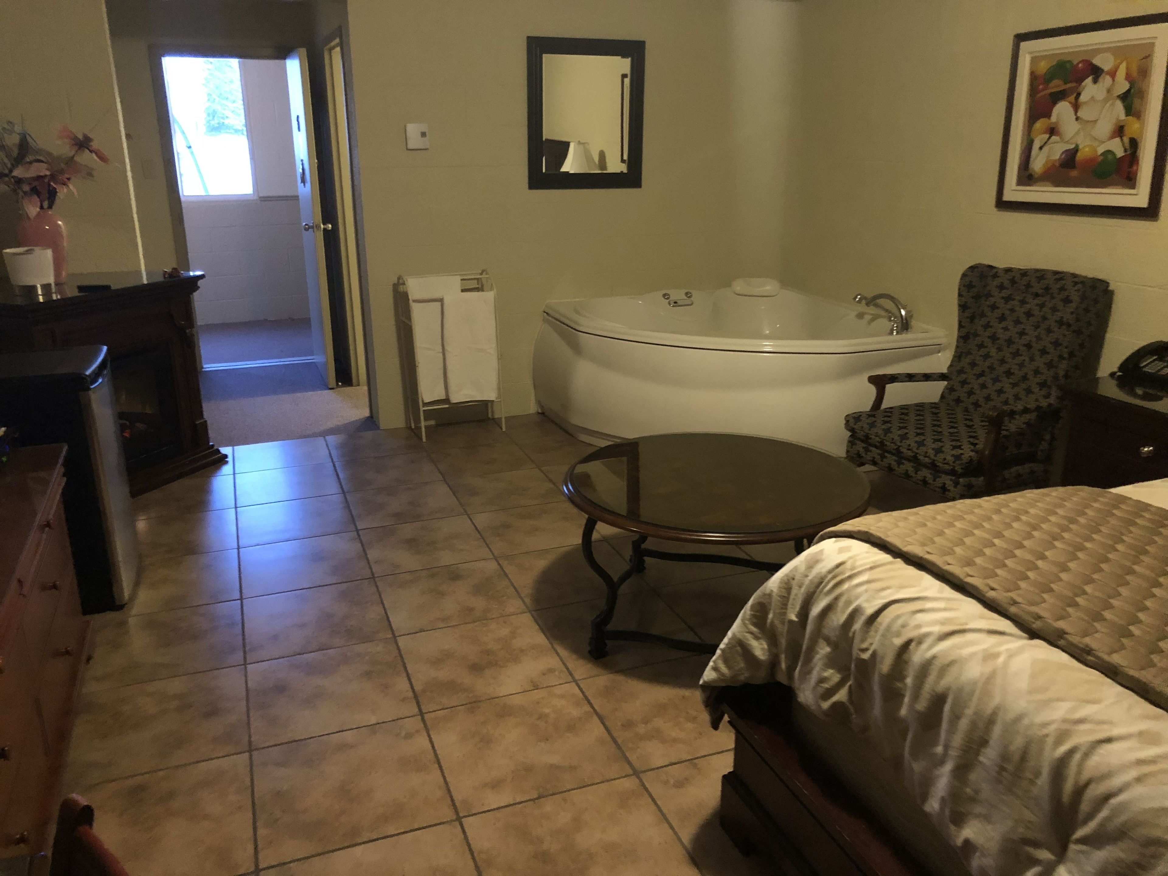 Une chambre d’hôtel avec un lit, une table ronde, une chaise, une baignoire, une commode, un miroir et un tableau accroché au mur.
