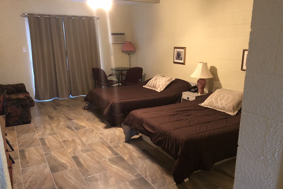 A hotel room with two beds, a chair, a small table, and a lamp.