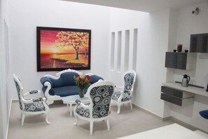 Ein Essbereich mit einem blauen Sofa, weißen Stühlen mit Muster und einem Gemälde von einem Sonnenuntergang.