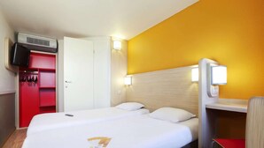 Une chambre d’hôtel avec un lit, une armoire rouge, une télévision et un bureau avec une chaise.