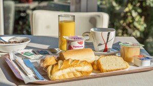 Un plateau de petit-déjeuner avec du pain, du beurre, de la confiture, un verre de jus d’orange, une tasse et un bol de céréales.