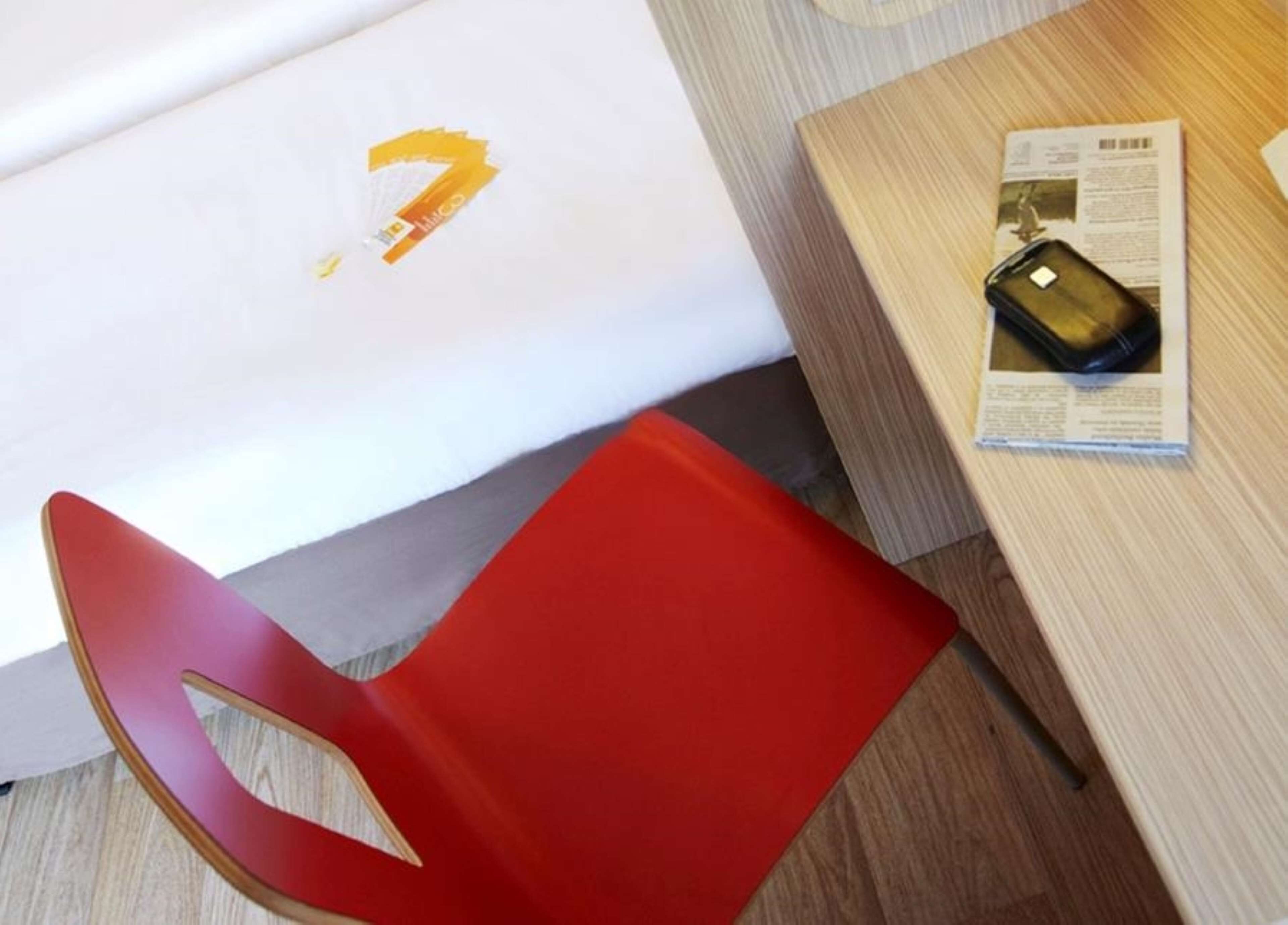 Une chaise rouge, une table en bois et un objet noir posé sur un journal.