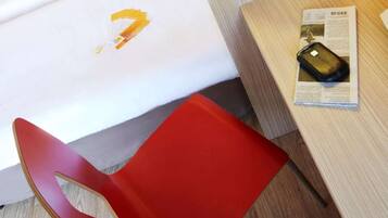 Une chaise rouge, une table en bois et un objet noir posé sur un journal.