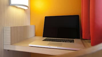 A laptop on a wooden desk in a room with a yellow wall and a red curtain.