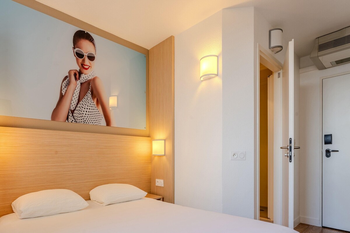 A hotel room with a bed, a wall-mounted mirror, and two bedside lamps.