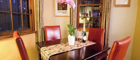 Et spisebord med et mønstret borddække, omgivet af røde læderstole. Der er en vase med blomster og en champagneflaske på bordet.