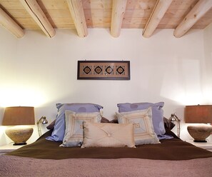 Ein Schlafzimmer mit Holzbalkendecke, einem Bett mit gemusterten Betttextilien und zwei Nachttischlampen.