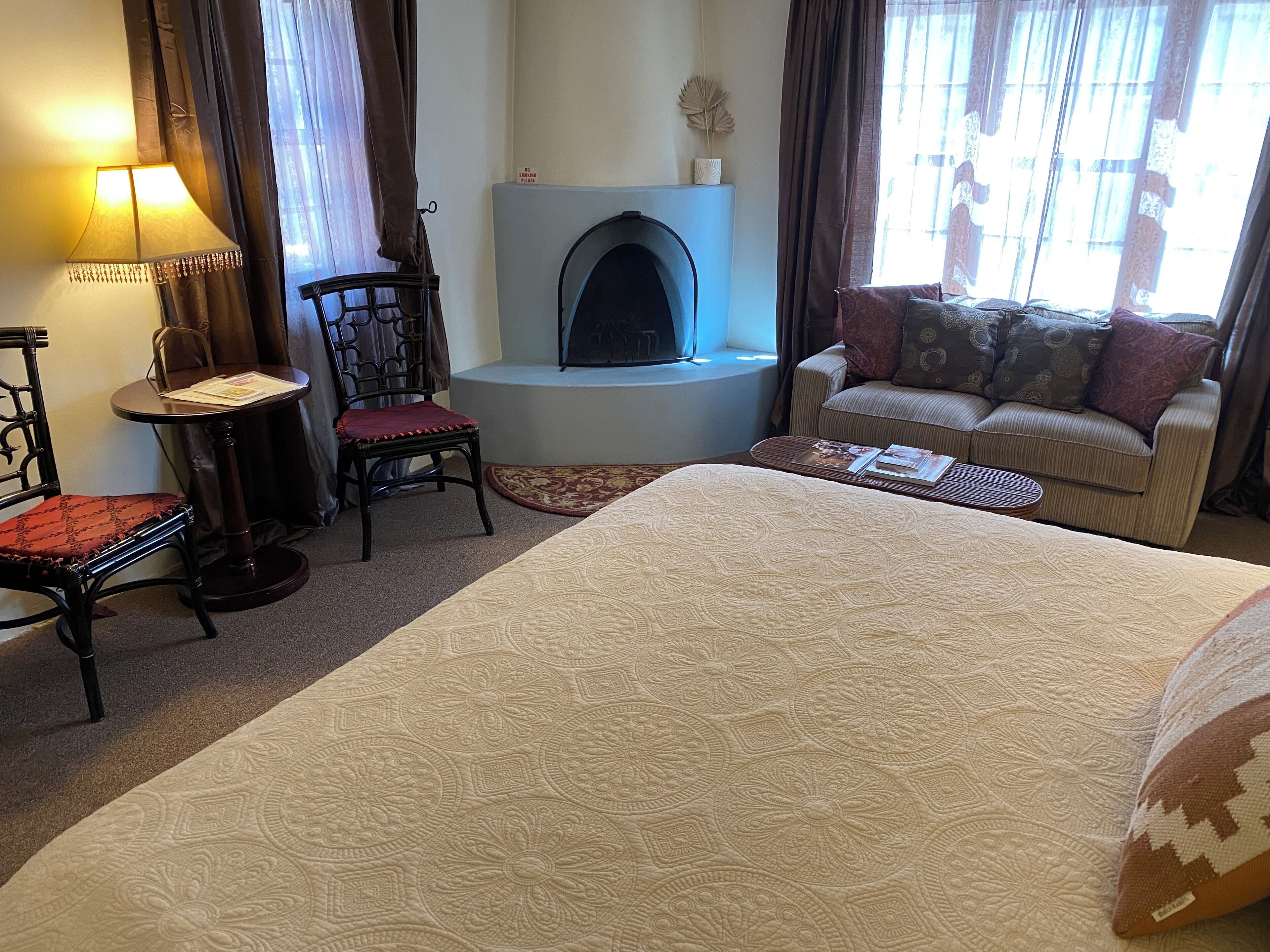 Habitación de hotel con una cama grande, un sofá, una silla, una mesita, una chimenea y una lámpara.