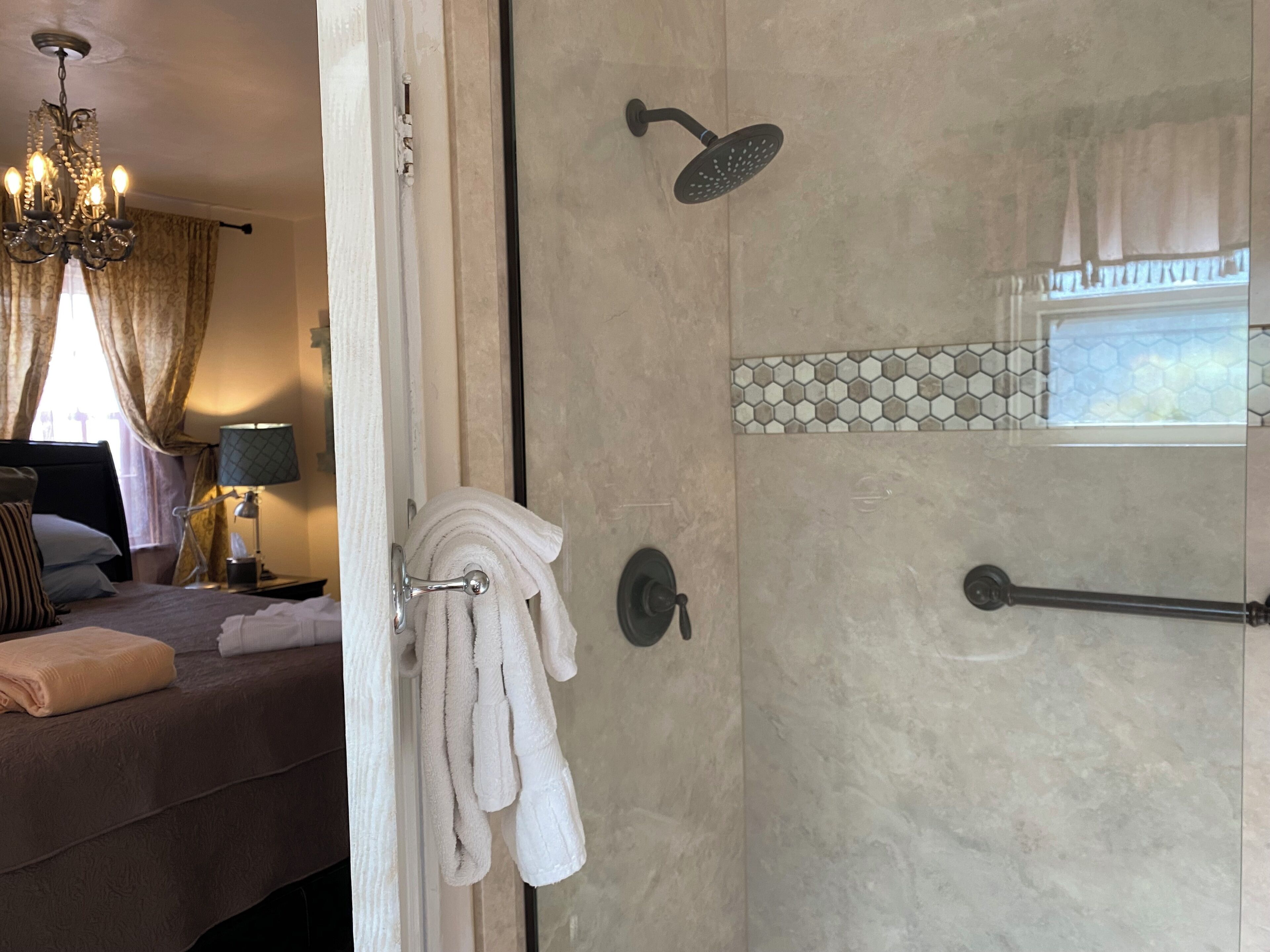 Ein Hotelzimmer mit Bett, einem Chandelier, einem Badezimmer mit Dusche und einem Fenster mit Vorhängen.