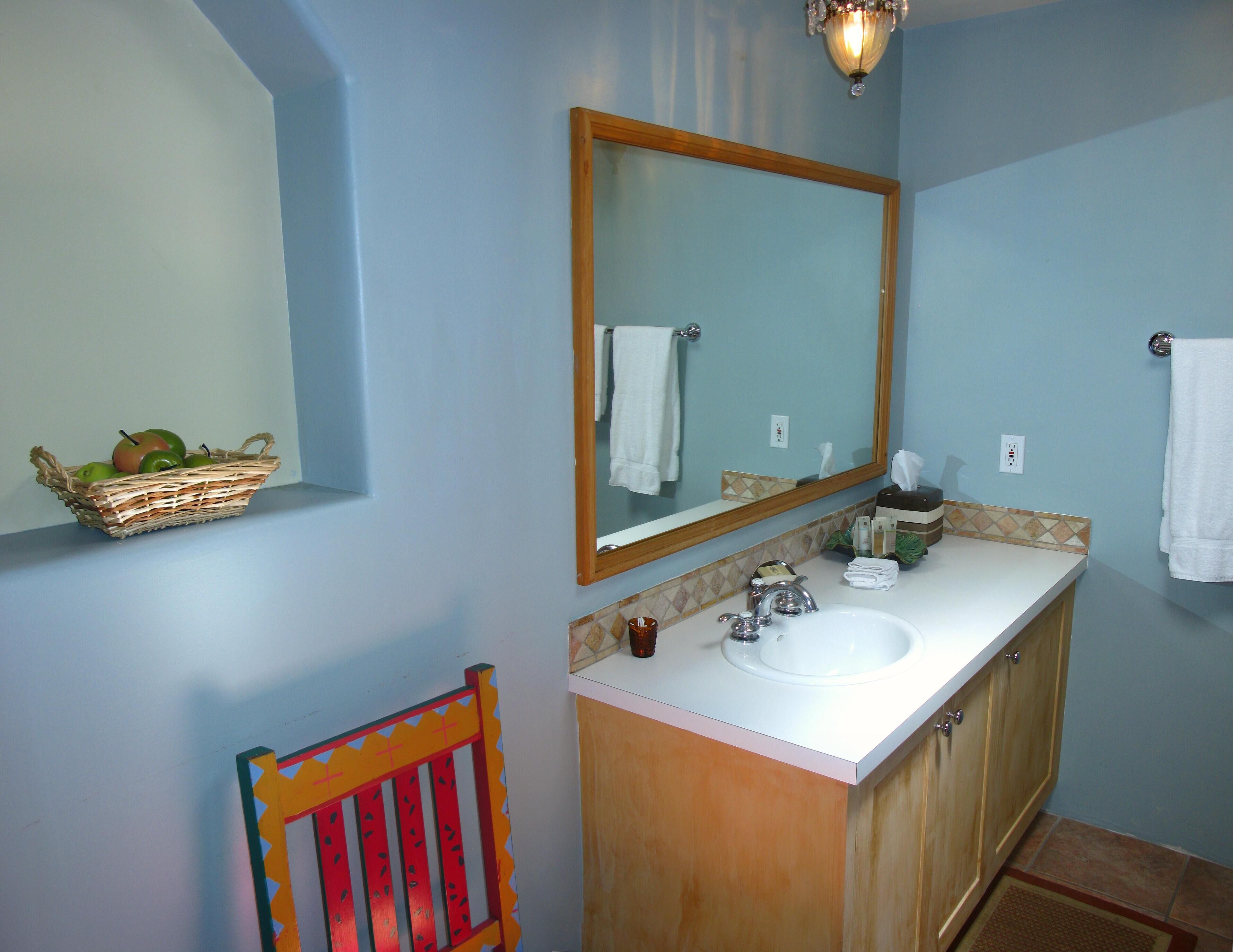 A bathroom with a sink, mirror, and a basket of apples on the wall.