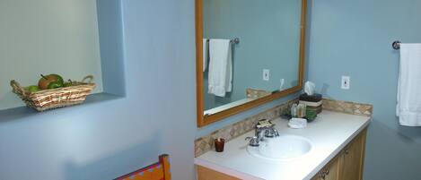 A bathroom with a sink, mirror, and a basket of apples on the wall.