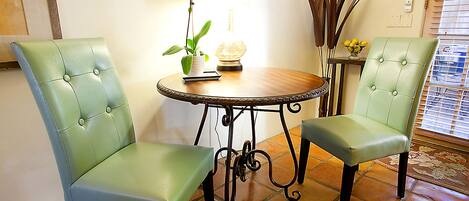 Two green upholstered chairs, a round wooden table with a potted orchid, and a decorative lamp.