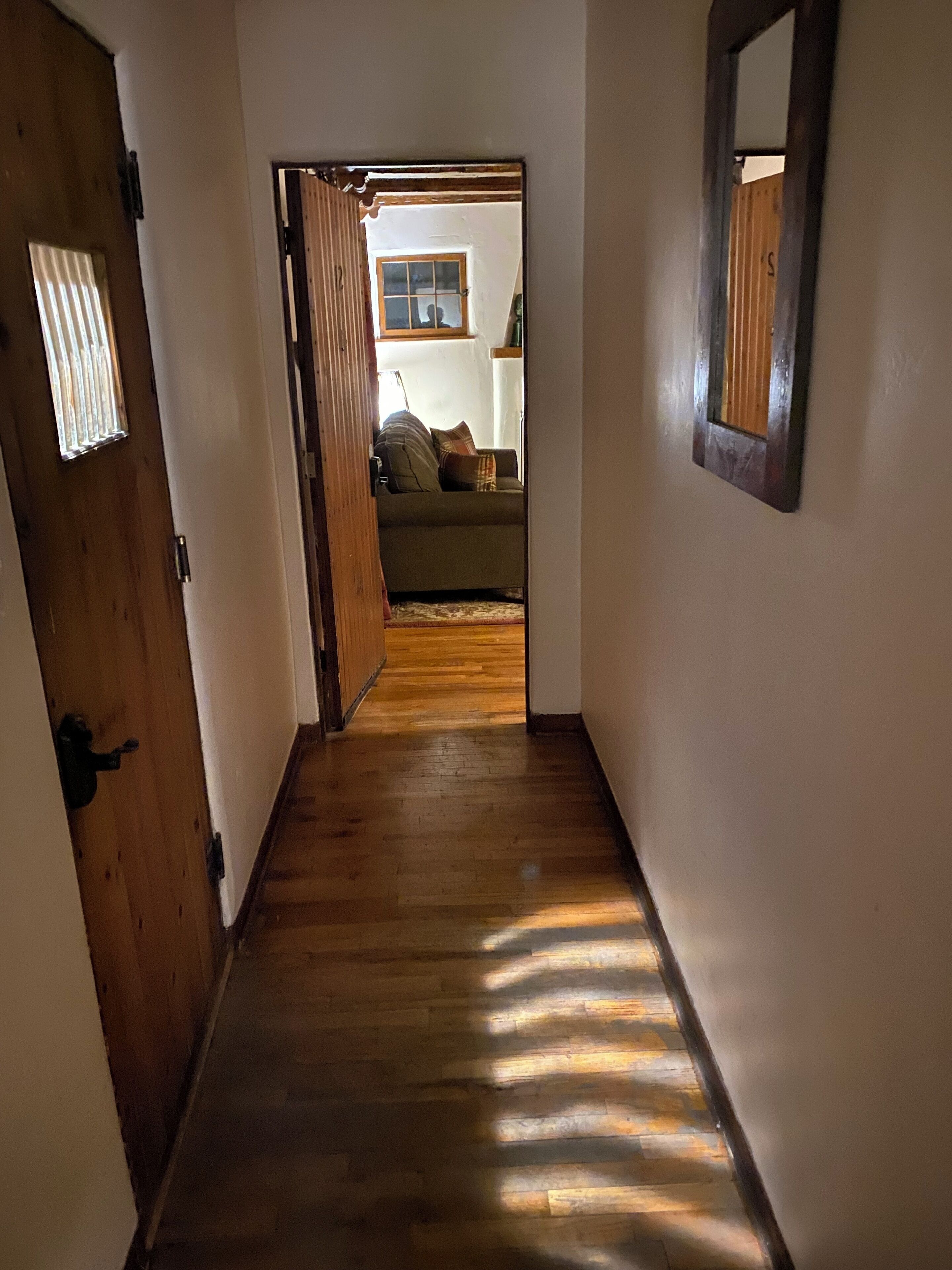 Un pasillo con piso de madera que conduce a una sala de estar con sofá y ventana.