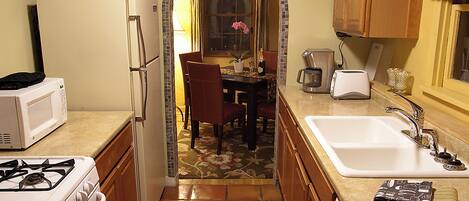 Une cuisine compacte équipée d’une cuisinière, d’un four à micro-ondes, d’un réfrigérateur et d’un évier. On y trouve également un coin repas avec des chaises et une table, ainsi qu’une fenêtre avec des rideaux.