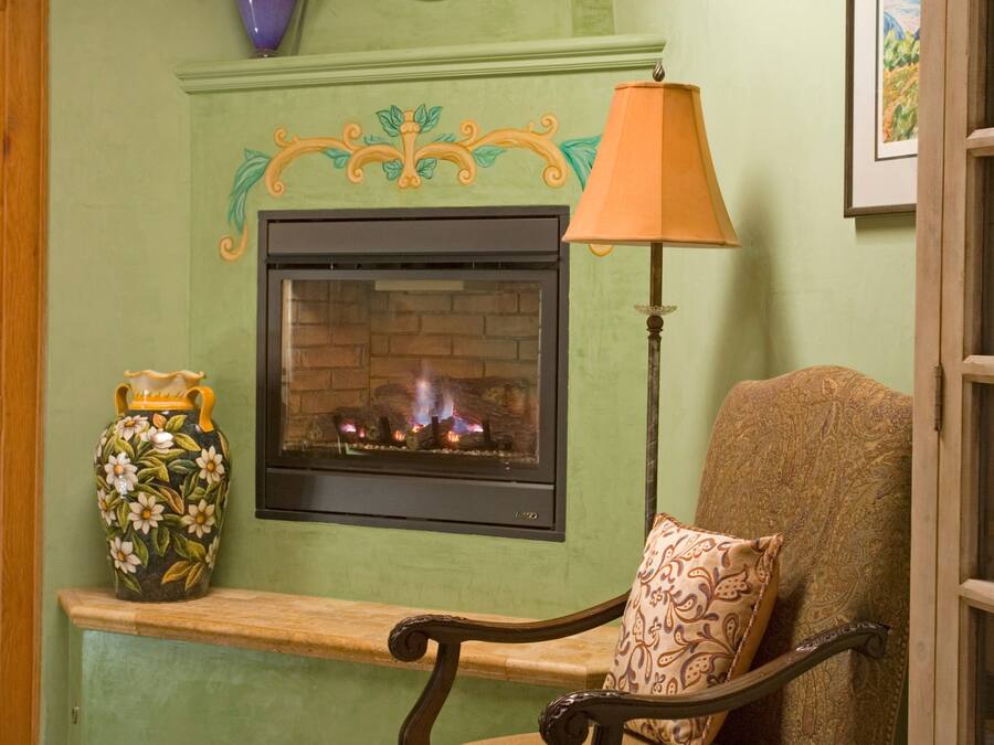 A cozy room with a fireplace, a chair with a patterned cushion, and decorative vases.