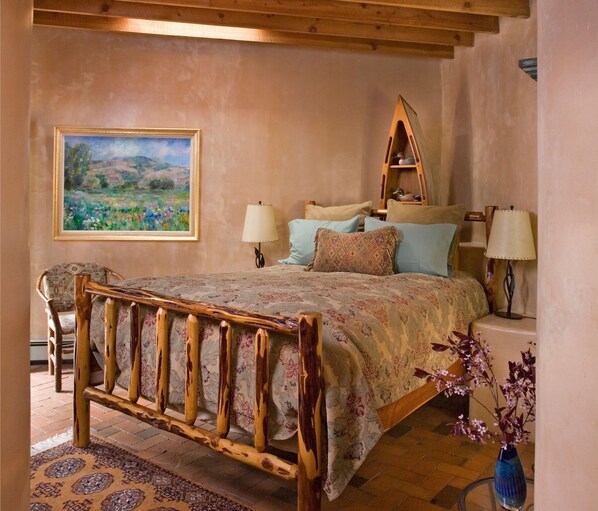 A bedroom with a wooden bed frame, a painting on the wall, and a nightstand with a lamp. - El Farolito Bed & Breakfast Inn (Santa Fe)