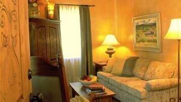 A cozy living room with a sofa, a table, and a lamp. There is a door on the left and a painting on the wall.