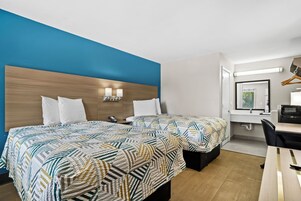 A hotel room with two beds, a desk, a chair, a mirror, and a bathroom.