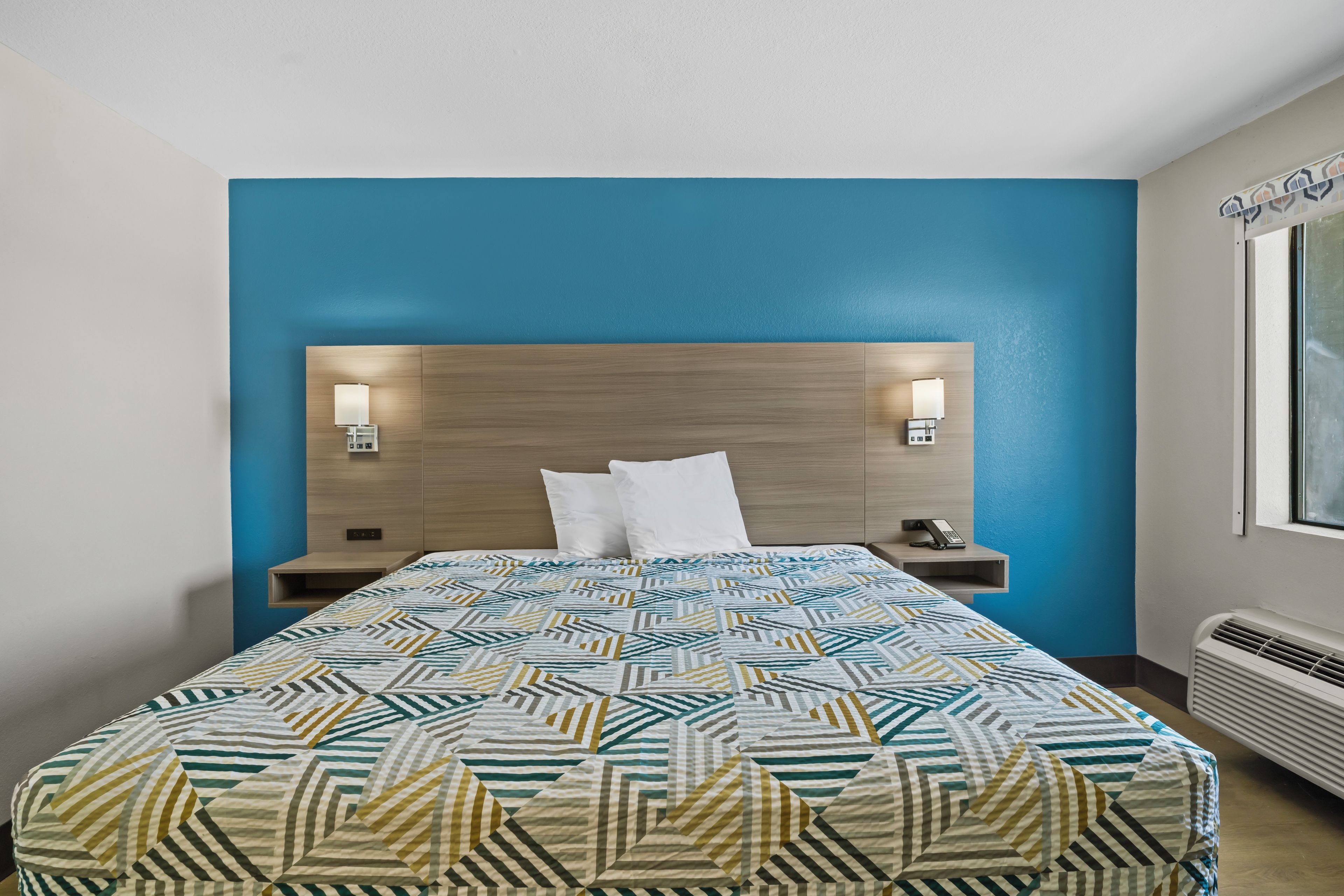 A hotel room with a bed, two bedside tables, a headboard, and a window.