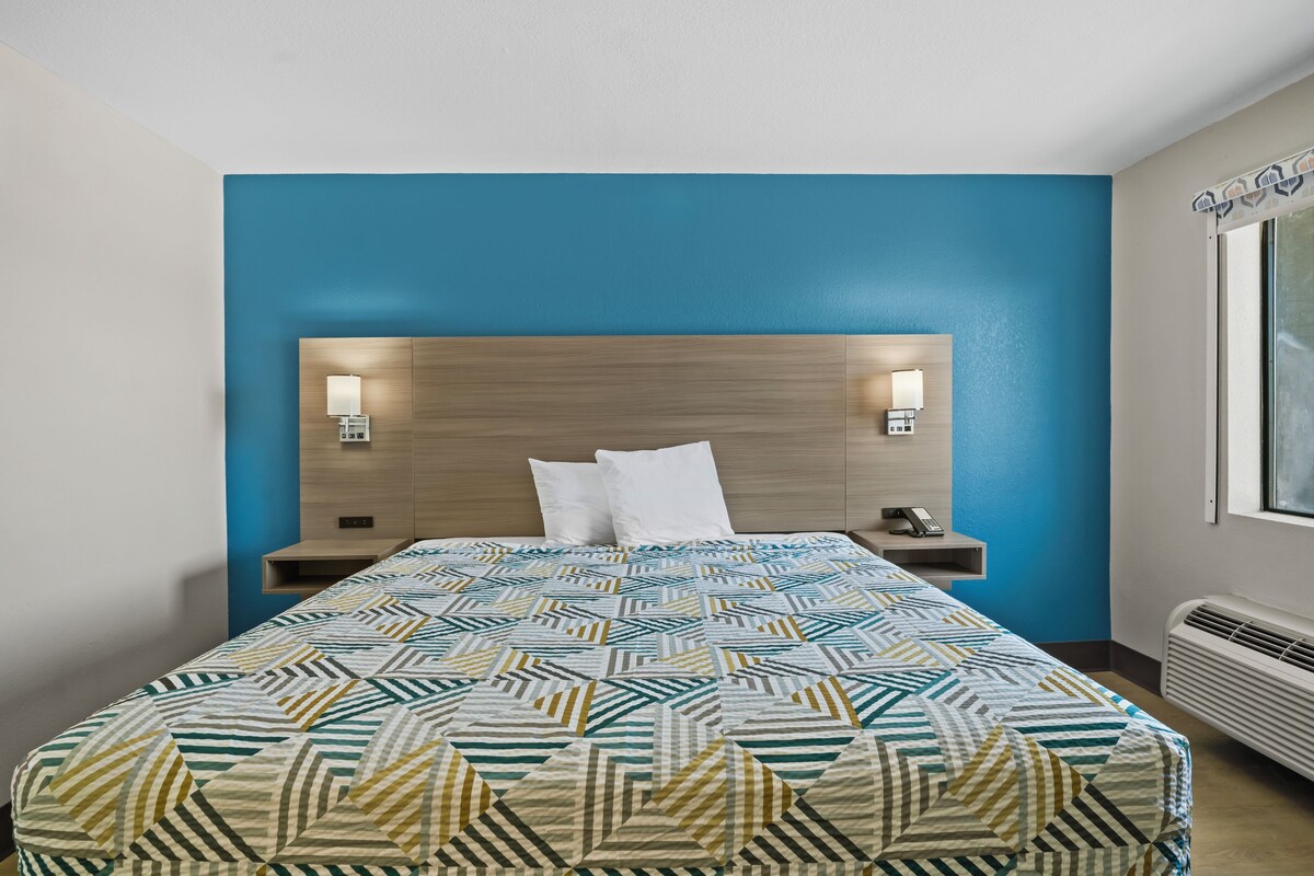 A hotel room with a bed, two bedside tables, a headboard, and a window.