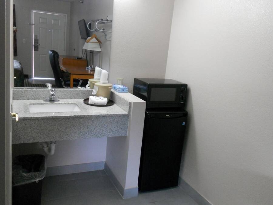 A compact bathroom with a sink, mirror, and a black microwave.